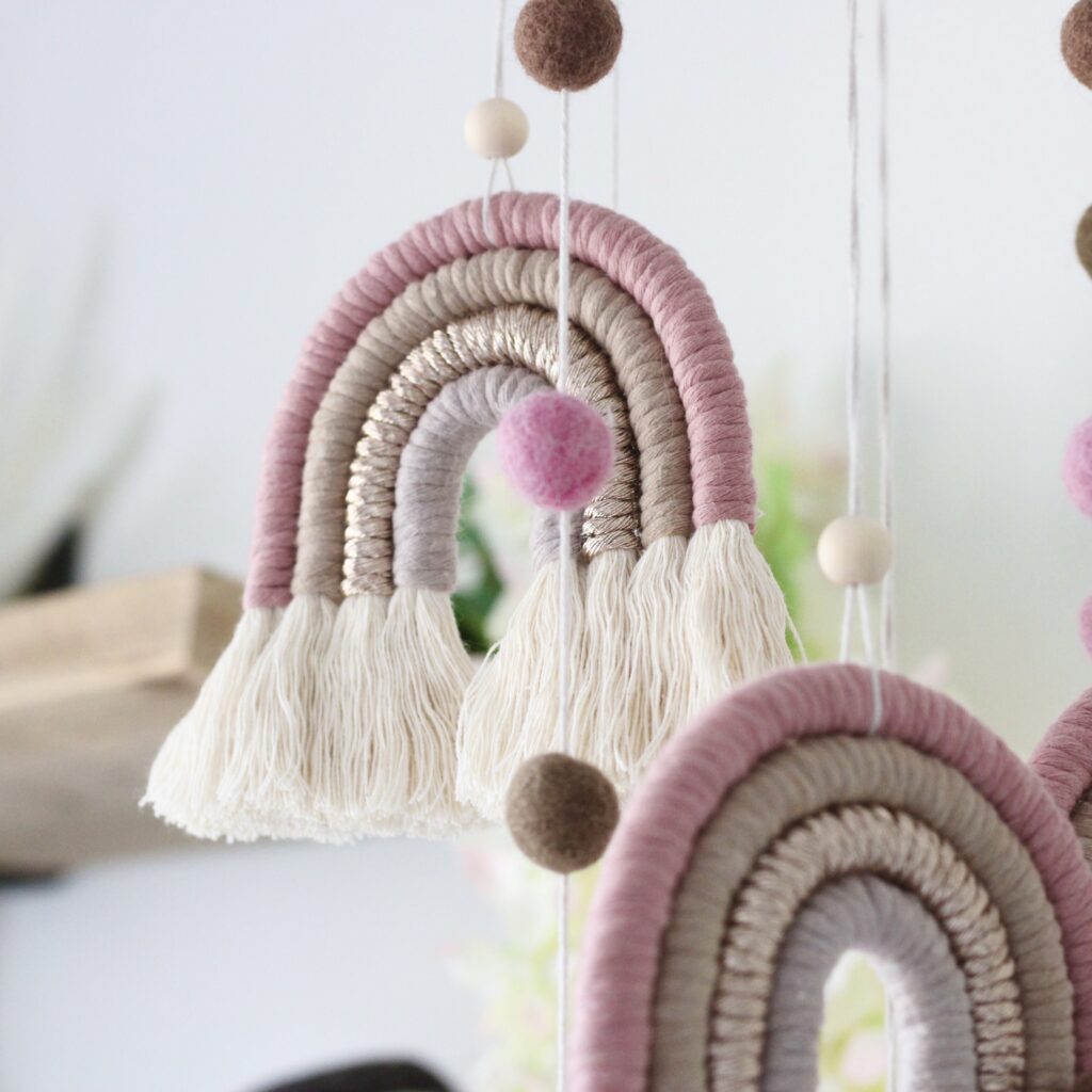 Piglet&Chestnut handmade rainbow macramé mobile with four macramé rainbows and cascading pompoms, hung from a wooden hoop